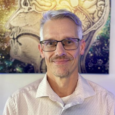 Man wearing glasses and light-colored shirt smiling.
