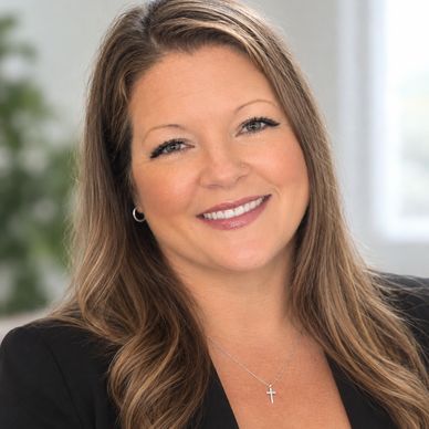 Smiling woman with long hair wearing a black blazer and cross necklace.