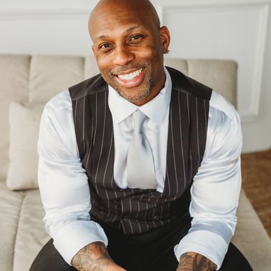 Smiling man in a vest sitting on a couch.