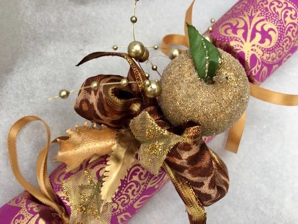 A damson and gold flocked Christmas cracker. A gold apple, gold leaves and leopard print bow on top