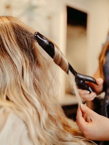Stylist curling blonde hair with a curling iron.
