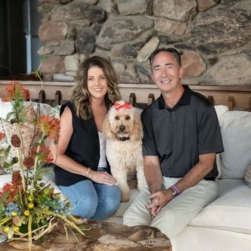 Couple sitting on a couch with their dog wearing a red bow.