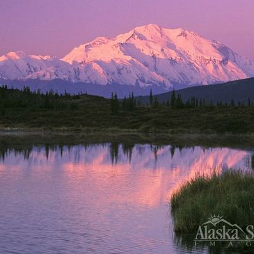 Snow-covered mountain reflecting in a serene lake at sunset.