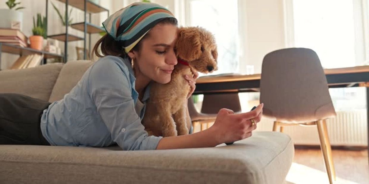 Woman lying on couch with dog, looking at phone.