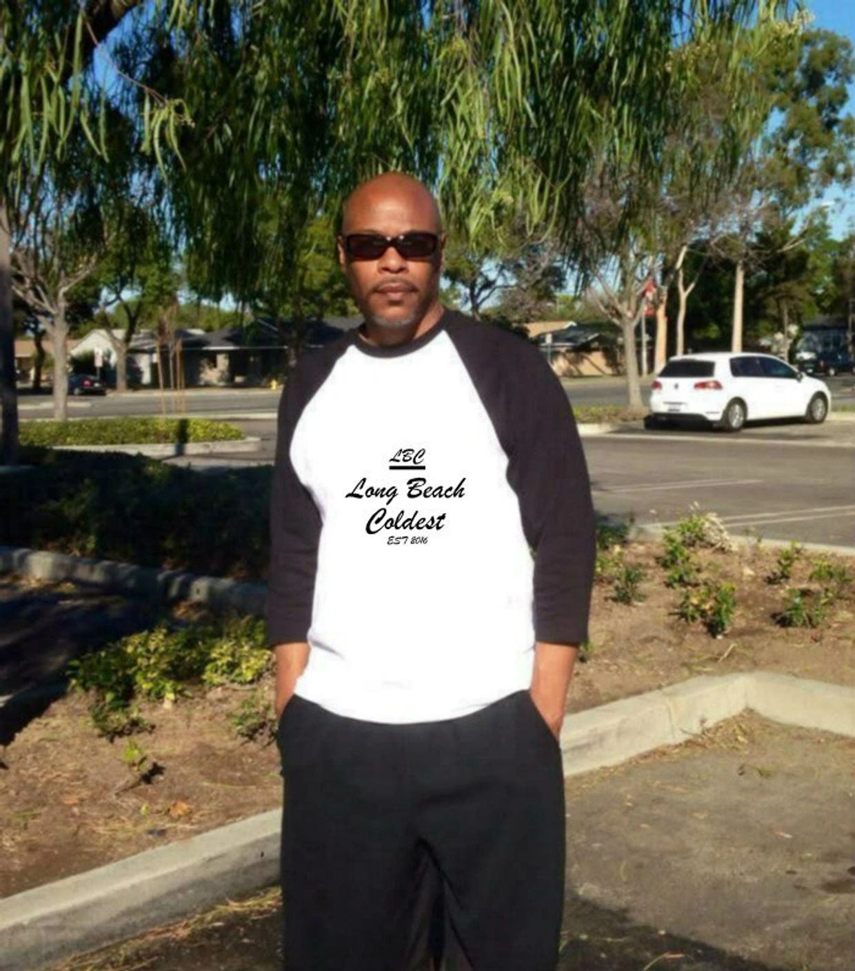 Man in sunglasses wearing Long Beach Coldest shirt outdoors.