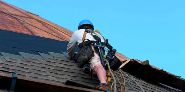 Worker with safety gear repairing a rooftop under clear blue sky.