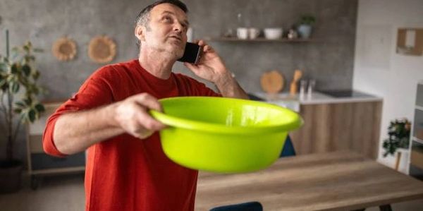 Man holding a green basin and talking on the phone in a kitchen.