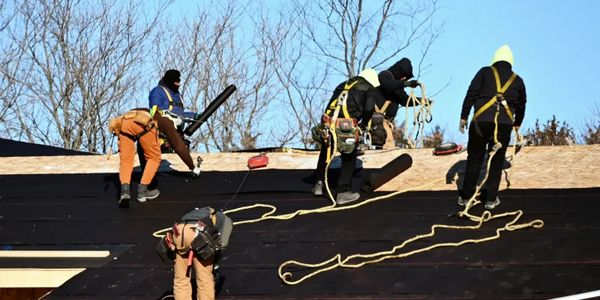 Construction workers installing roofing material on a house under clear blue sky.