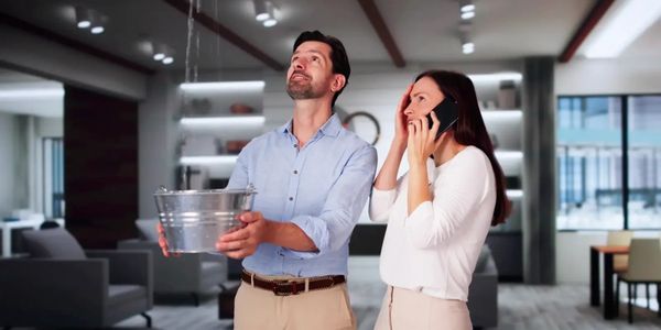 Couple dealing with indoor water leak using a bucket and phone.