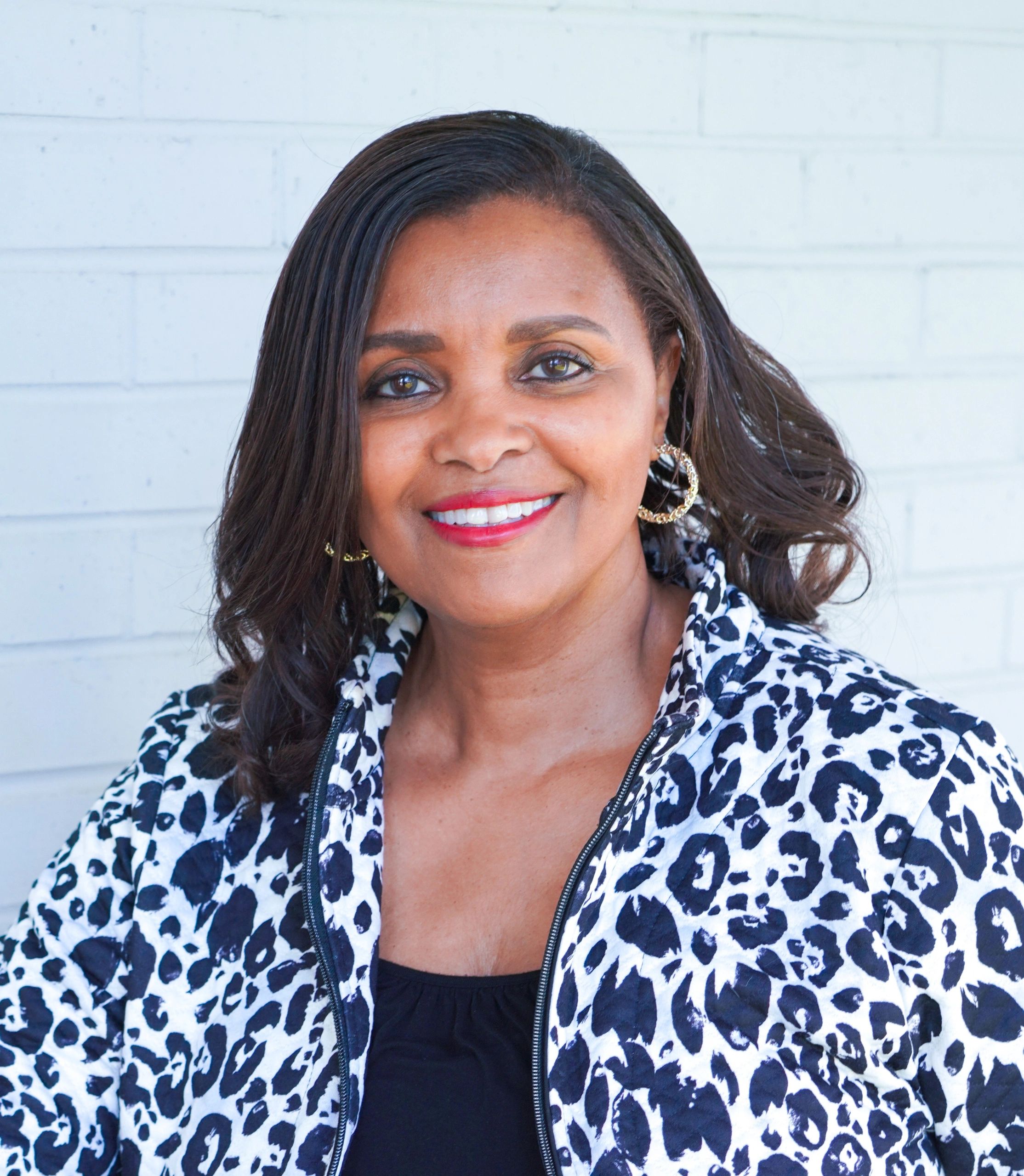 Smiling woman in leopard print jacket against white brick wall.