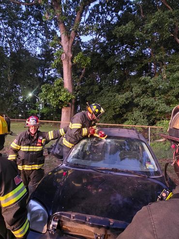 Firefighters practicing car rescue techniques on a damaged vehicle.