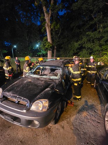 Firefighters inspecting a damaged car at night after an accident.