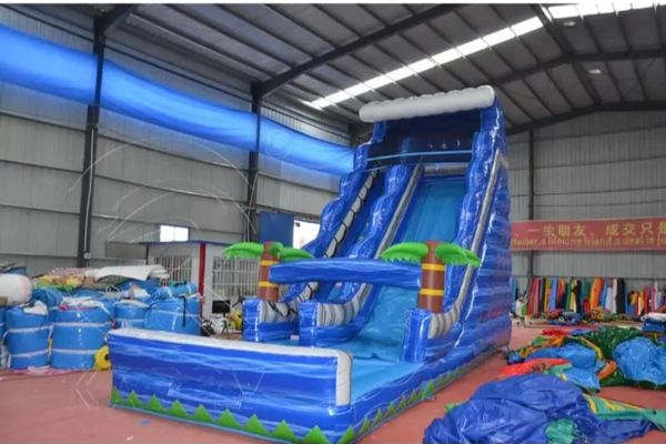 Large blue inflatable water slide with palm tree decorations indoors.