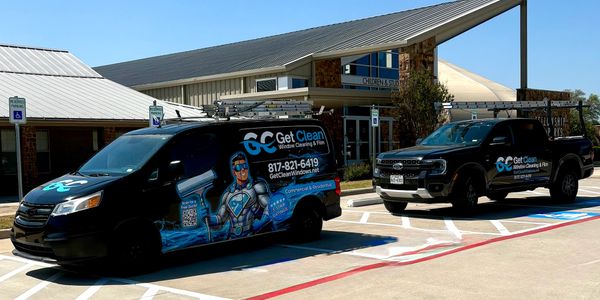 Two black vehicles with Get Clean window cleaning and pressure washing branding parked outside a building.