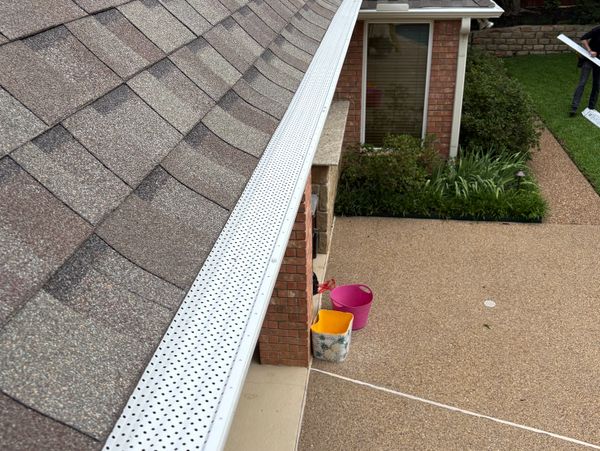 Newly installed white perforated gutter guard on a shingled roof.