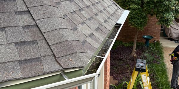 A house gutter being cleaned with a ladder and tools nearby.