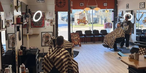 A busy barbershop with two customers getting haircuts in striped capes.