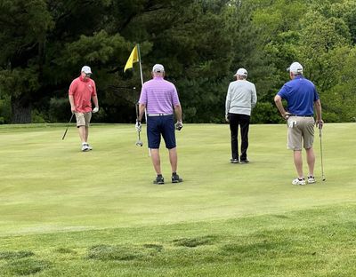 Four men playing golf on a green with a yellow flag.