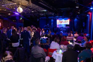 Audience gathered in a dimly lit club with a stage and live band setup.