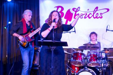 A band performs live at BJsicles with a singer, bassist, and drummer on stage.