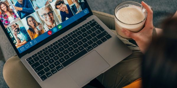 Person holding a drink during a video call on a laptop.
