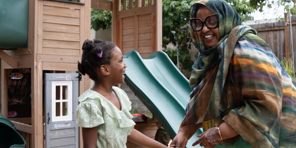A joyful child and woman holding hands near a playground slide outdoors.