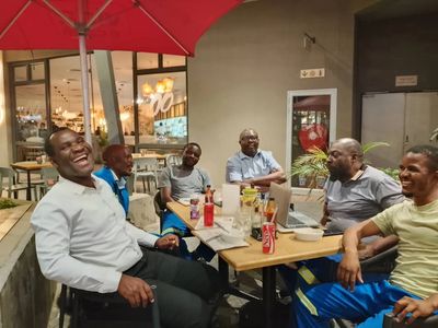 Group of men enjoying a lively conversation at an outdoor cafe under a red umbrella.