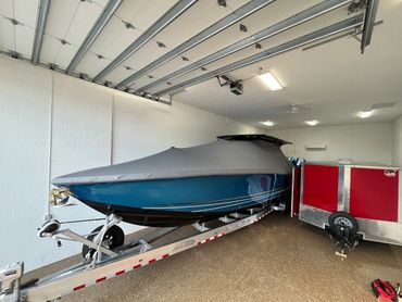 A covered blue boat on a trailer parked inside a garage with white walls.
