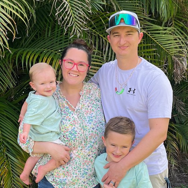 Happy family of four posing outdoors with greenery in the background.
