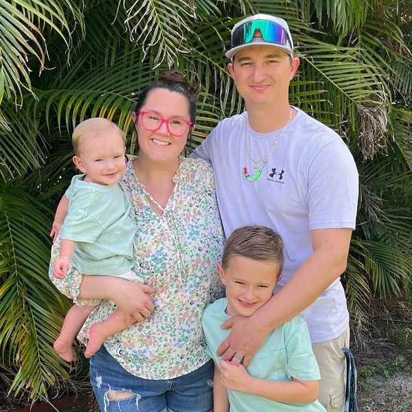 Happy family of four posing outdoors with greenery in the background.