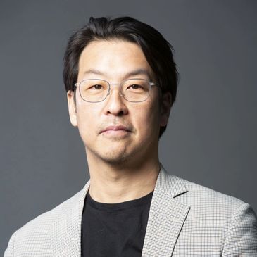 Portrait of a man wearing glasses and a checked blazer against a gray background.