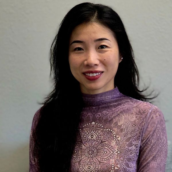Smiling woman with long black hair and purple patterned top.