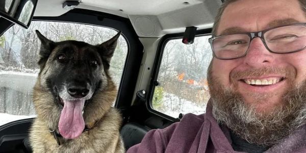 Man and dog smiling inside a vehicle in snowy weather.