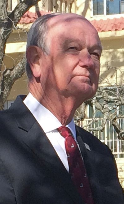 Elderly man in a suit standing outdoors with shadows on his face.