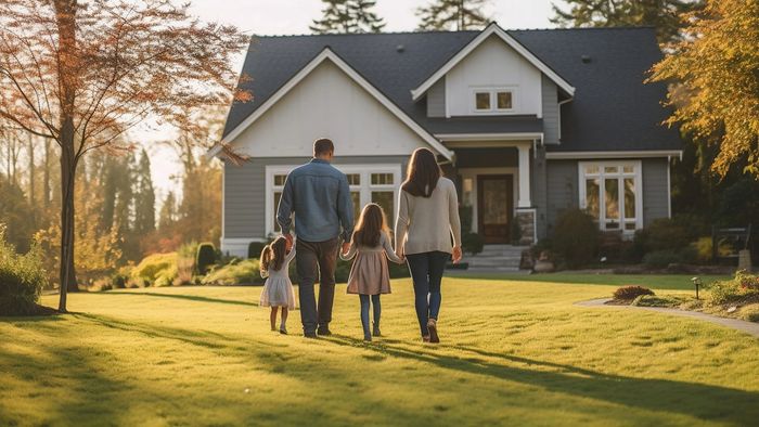 a family walking toward a modern gray home with green lawn and trees in the background