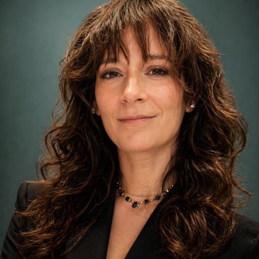 Professional woman with curly hair smiling softly against a dark background.