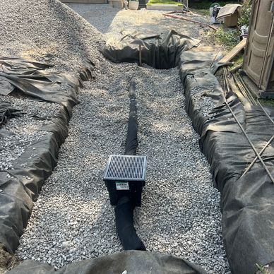 A gravel-filled trench with a drainage pipe and grate installed.
