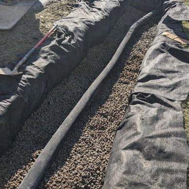 Drainage pipe laid in a trench filled with gravel and covered with fabric.
