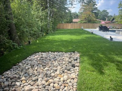 A backyard with green grass, a stone bed, and a patio area with furniture.