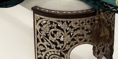 Intricately carved wooden stool with floral patterns and a green embroidered cloth draped over it.