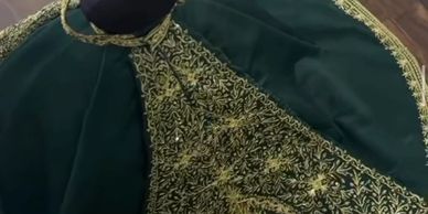 Green and gold embroidered cape displayed on a mannequin.