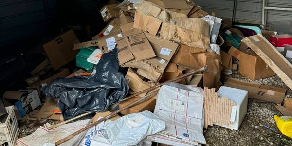 A large pile of flattened cardboard boxes and packages in a cluttered storage area.