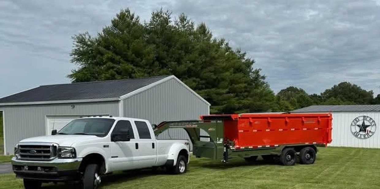 White pickup truck towing a large red trailer on grass near sheds.