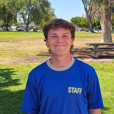 Young man smiling outdoors wearing a blue staff shirt.