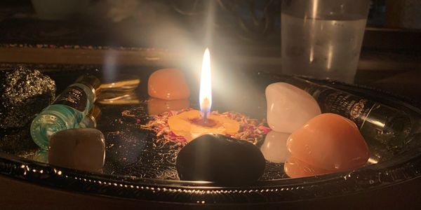 A lit candle surrounded by crystals and essential oils on a decorative tray.