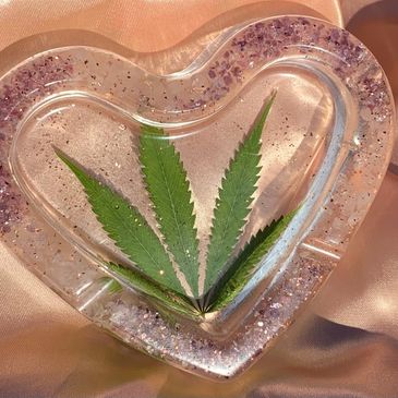 Heart-shaped resin tray with a green leaf embedded inside on a satin fabric.