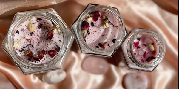 Three jars of pink floral candles on a silky fabric with stones.