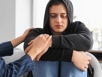 A woman comforting a sad young man in a hoodie.