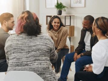 Group of five diverse people sitting in a circle, engaging in a friendly conversation.