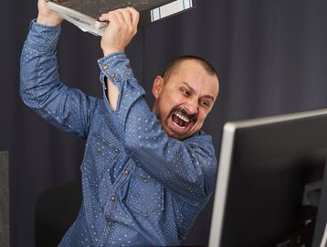 Angry man about to smash a computer monitor with a folder.